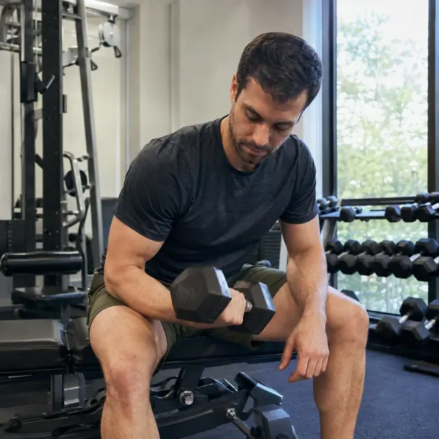 A man lifting a dumbbell on a workout bench in a gym